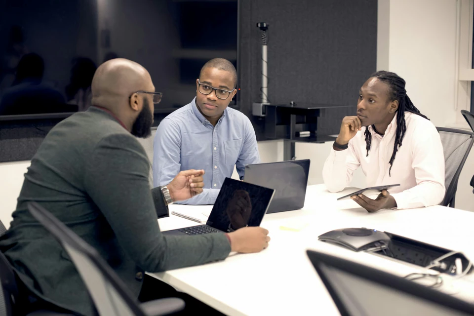 A group of people sitting around a table with laptops.