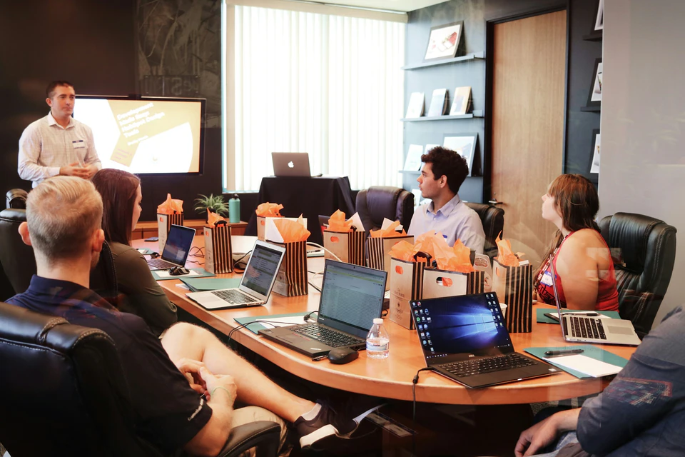 Man standing in front of people sitting beside table with laptop computers.